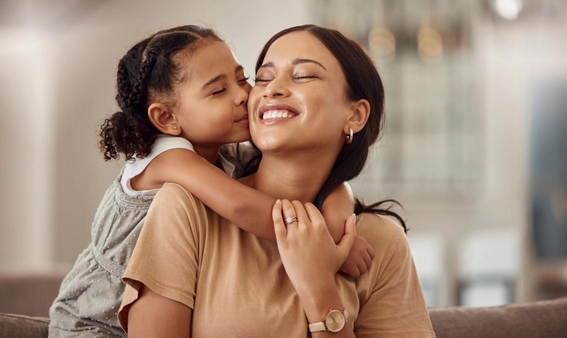 a little girl is kissing her mother on the cheek while sitting on a couch .