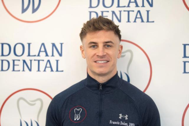Francis Dolan, DMD, smiling in front of Dolan Dental branding.