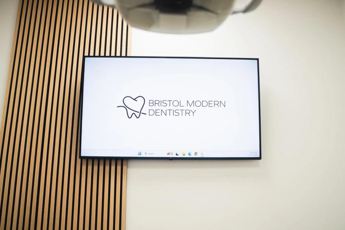 A wall-mounted TV screen displays the Bristol Modern Dentistry logo and name, next to a wooden slatted panel.