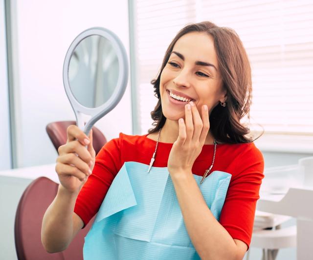 a woman is looking at her teeth in a mirror at the dentist .