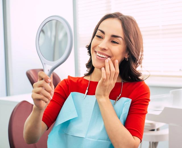 a woman is looking at her teeth in a mirror at the dentist .