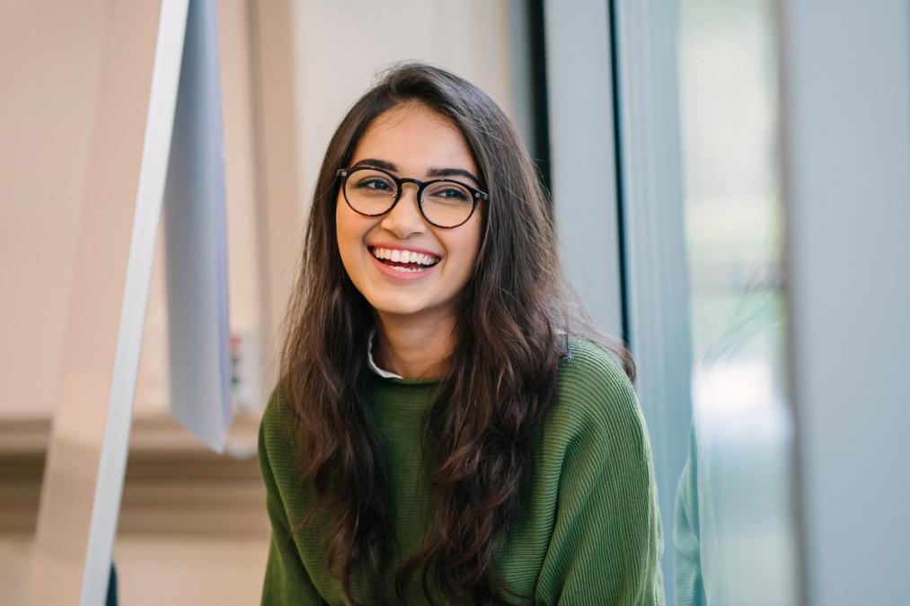 a young woman wearing glasses and a green sweater is smiling for the camera .