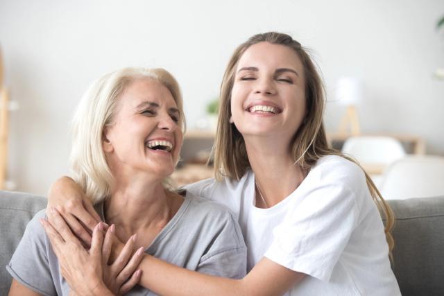 a young woman is hugging an older woman on a couch and they are laughing .