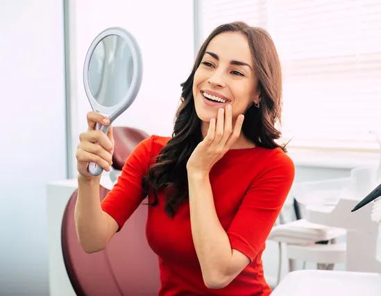 a woman is smiling while looking at her teeth in a mirror .