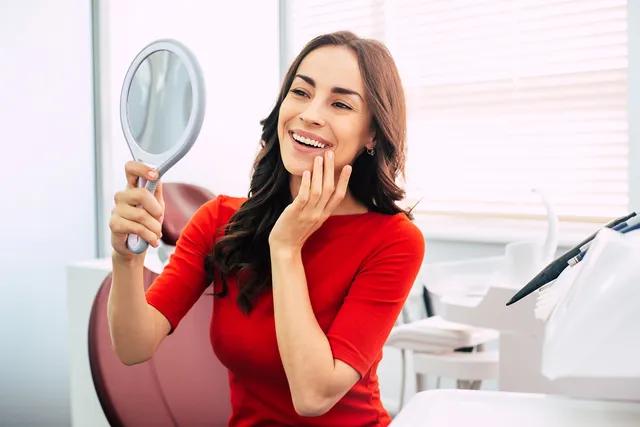 a woman is smiling while looking at her teeth in a mirror .