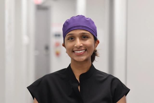 a woman wearing a purple scrub cap and a black shirt is smiling for the camera .