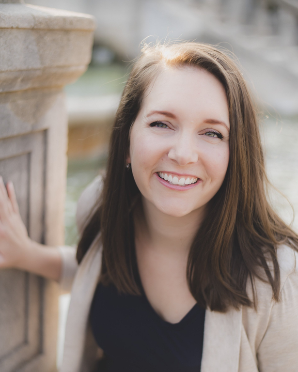 a woman is smiling and leaning against a stone wall