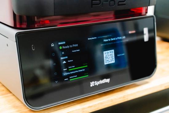 A SprintRay Pro 2 3D printer with its touchscreen display showing "Ready to Print" status and a QR code for sending print jobs.