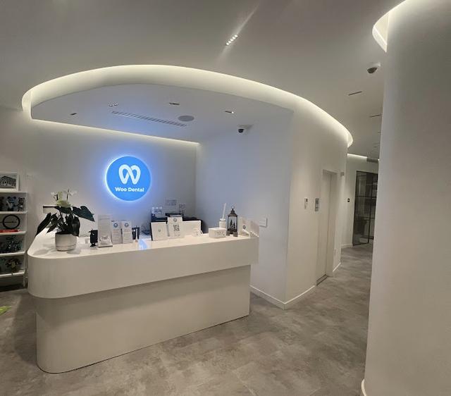 a white reception desk in a dental office with a blue logo on the wall .