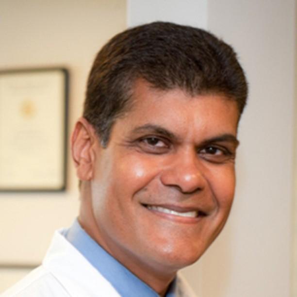 a man in a white coat and blue shirt smiles for the camera
