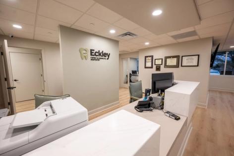 A modern dental office reception area with a reception desk and the Eckley Family & Cosmetic Dentistry logo on the wall.