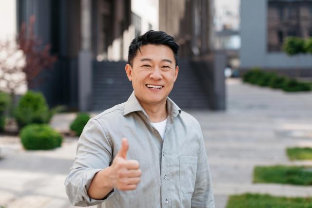 a man is giving a thumbs up sign while standing in front of a building .