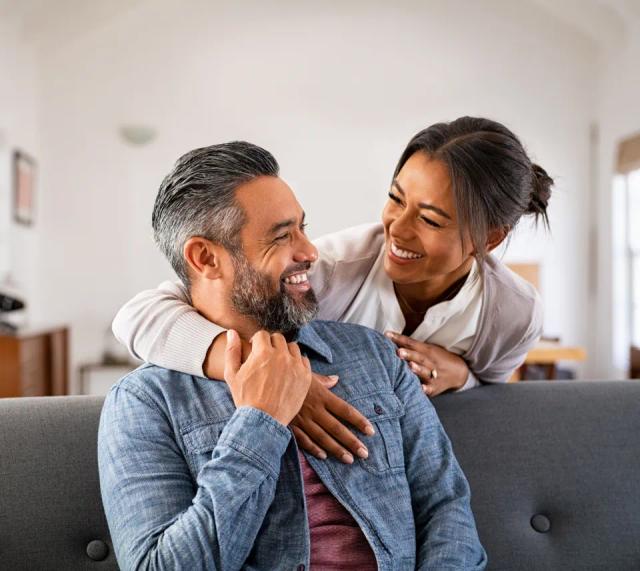 a woman is hugging a man on a couch and they are smiling at each other .