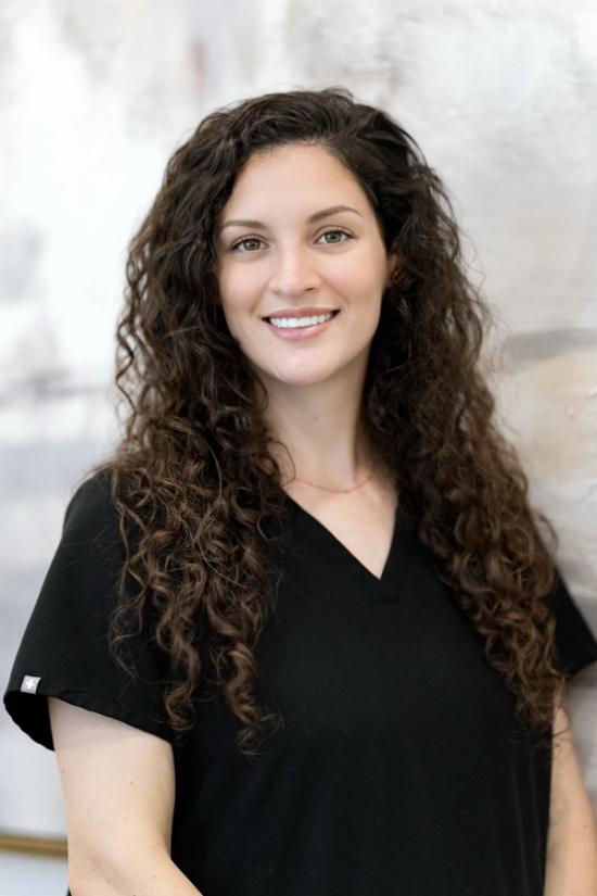a woman with curly hair is wearing a black scrub top and smiling .