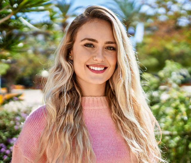 a beautiful young blonde woman wearing a pink sweater is smiling and looking at the camera .