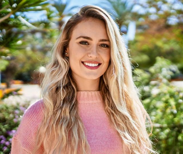 a beautiful young blonde woman wearing a pink sweater is smiling and looking at the camera .