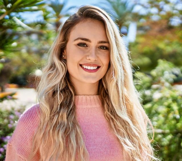 a beautiful young blonde woman wearing a pink sweater is smiling and looking at the camera .