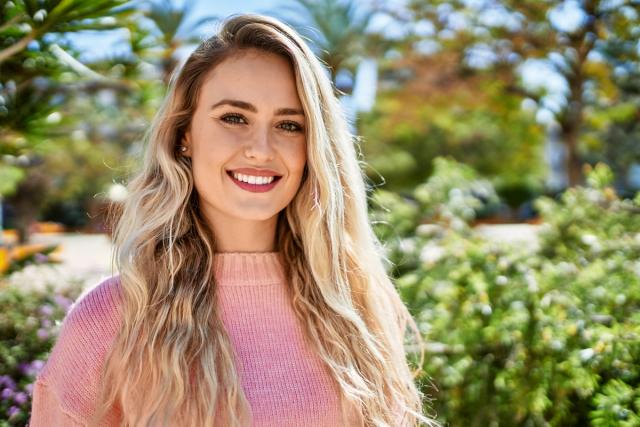 a beautiful young blonde woman wearing a pink sweater is smiling and looking at the camera .