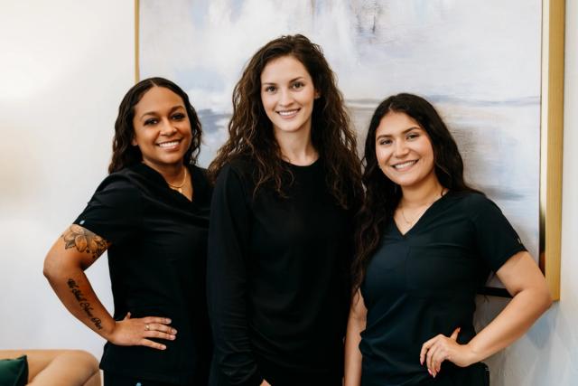 three women are posing for a picture together in front of a painting .