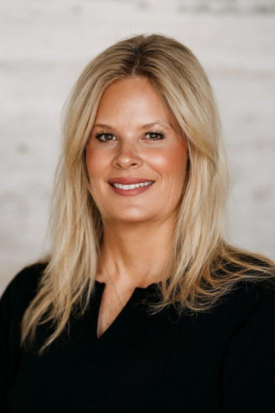 Headshot of a smiling woman with blonde hair wearing a black top.