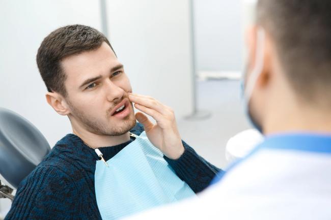 a man is sitting in a dental chair holding his mouth in pain .