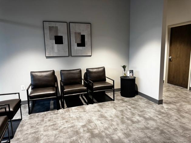 Waiting room with dark chairs, two abstract wall art pieces, and a small side table.