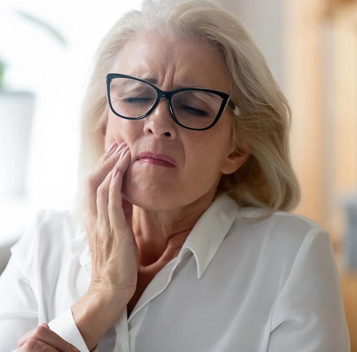 an older woman wearing glasses is holding her mouth in pain .