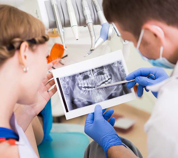 A dentist points to a dental X-ray as a patient looks on, with dental tools in the background.