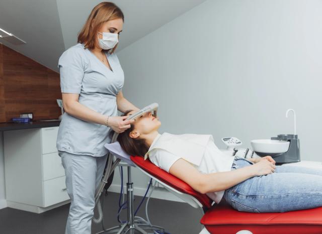 A dental professional adjusts a sedation mask on a patient in a dental chair.