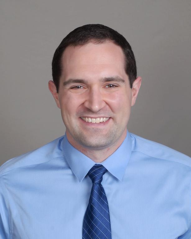 Smiling man in a blue shirt and striped tie.
