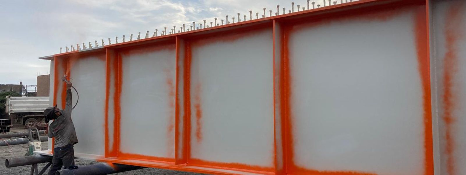 Operario aplicando recubrimiento industrial a soplete sobre una viga armada de acero