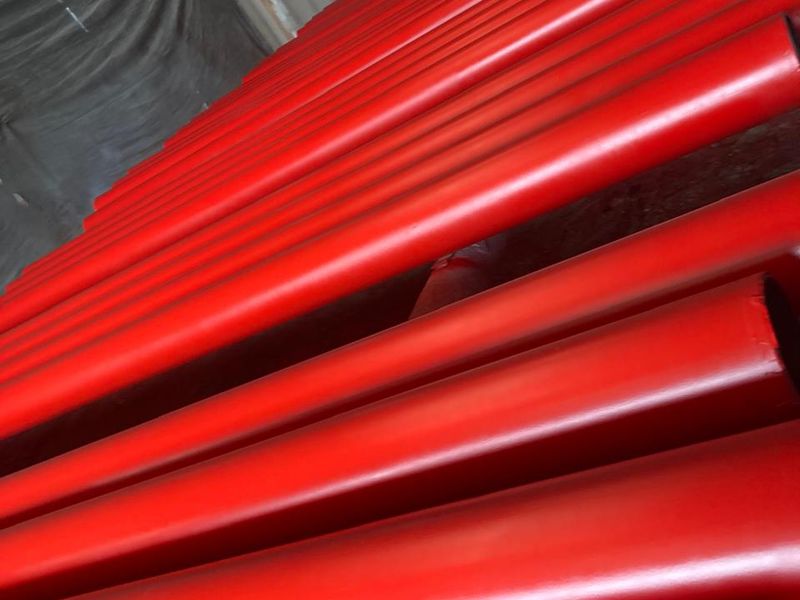 Tuberías de acero con recubrimiento rojo-naranja apiladas en el taller