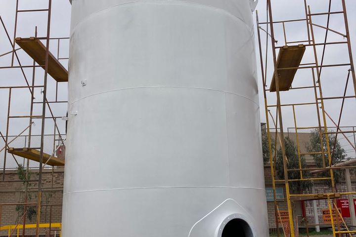 Tanque de almacenamiento vertical con acabado recién aplicado, con andamios y boca de hombre en la base