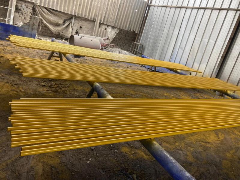 Perfiles de fibra de vidrio con recubrimiento amarillo, apilados en el taller