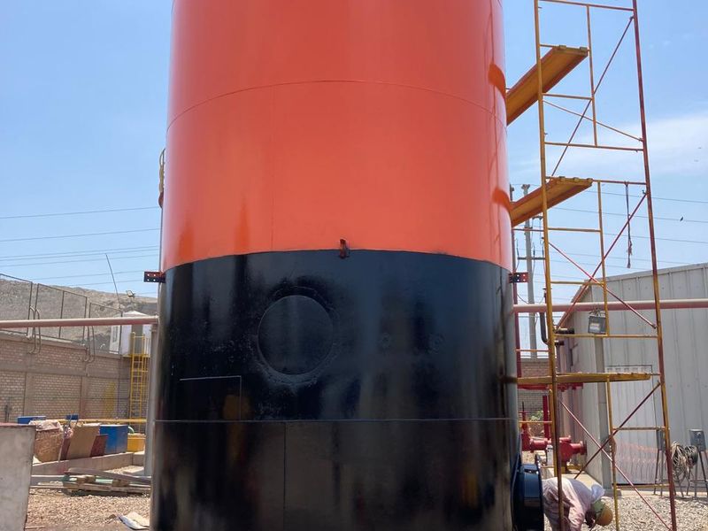 Recipiente vertical de acero con acabado naranja y negro, con andamio para su terminación