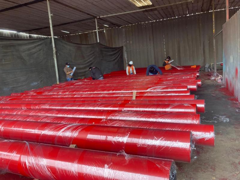 Tuberías con recubrimiento rojo-naranja embaladas, con la cuadrilla en el taller