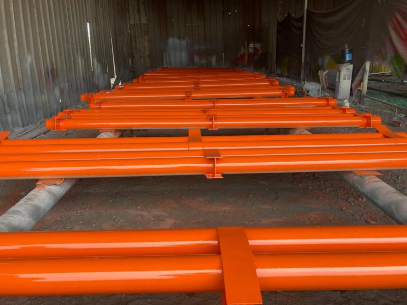 Vigas estructurales con recubrimiento naranja alineadas en perspectiva en el taller