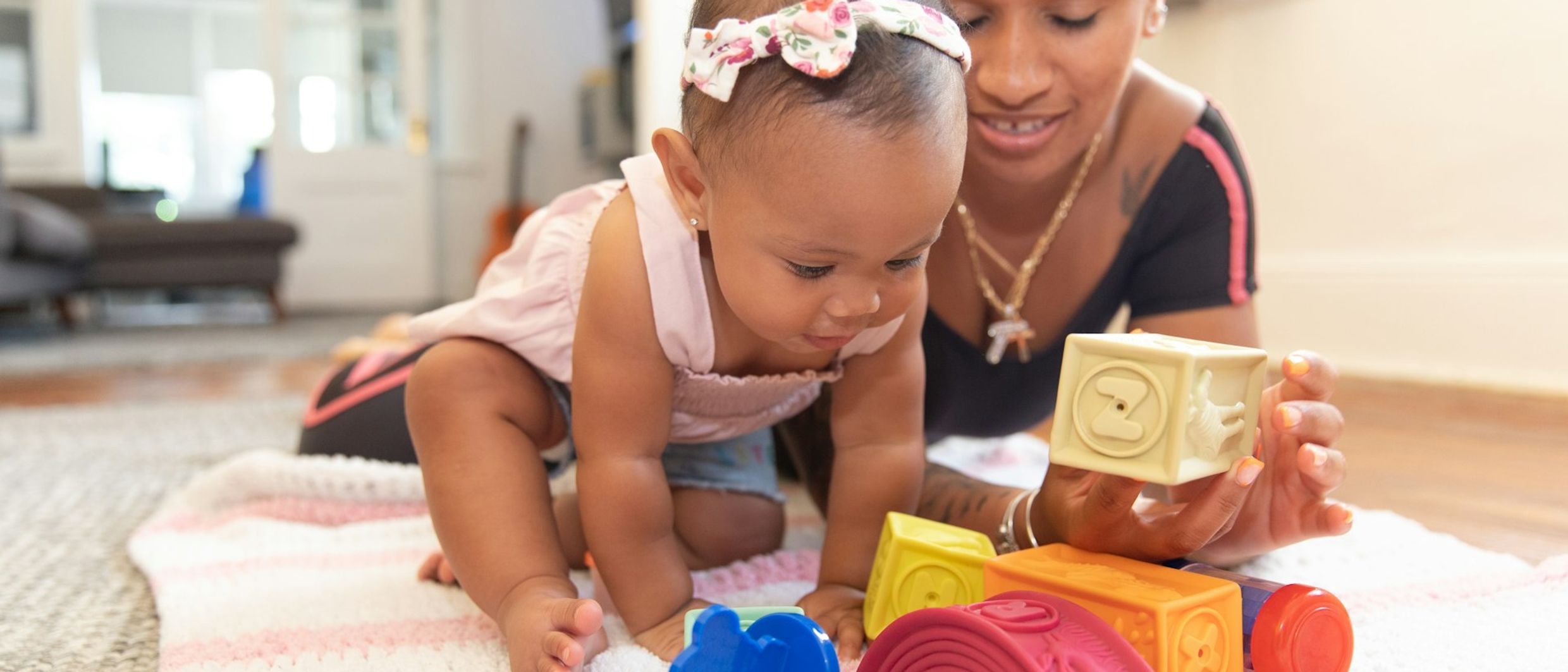 A mother sitting on a blanket playing with toys alongside her baby