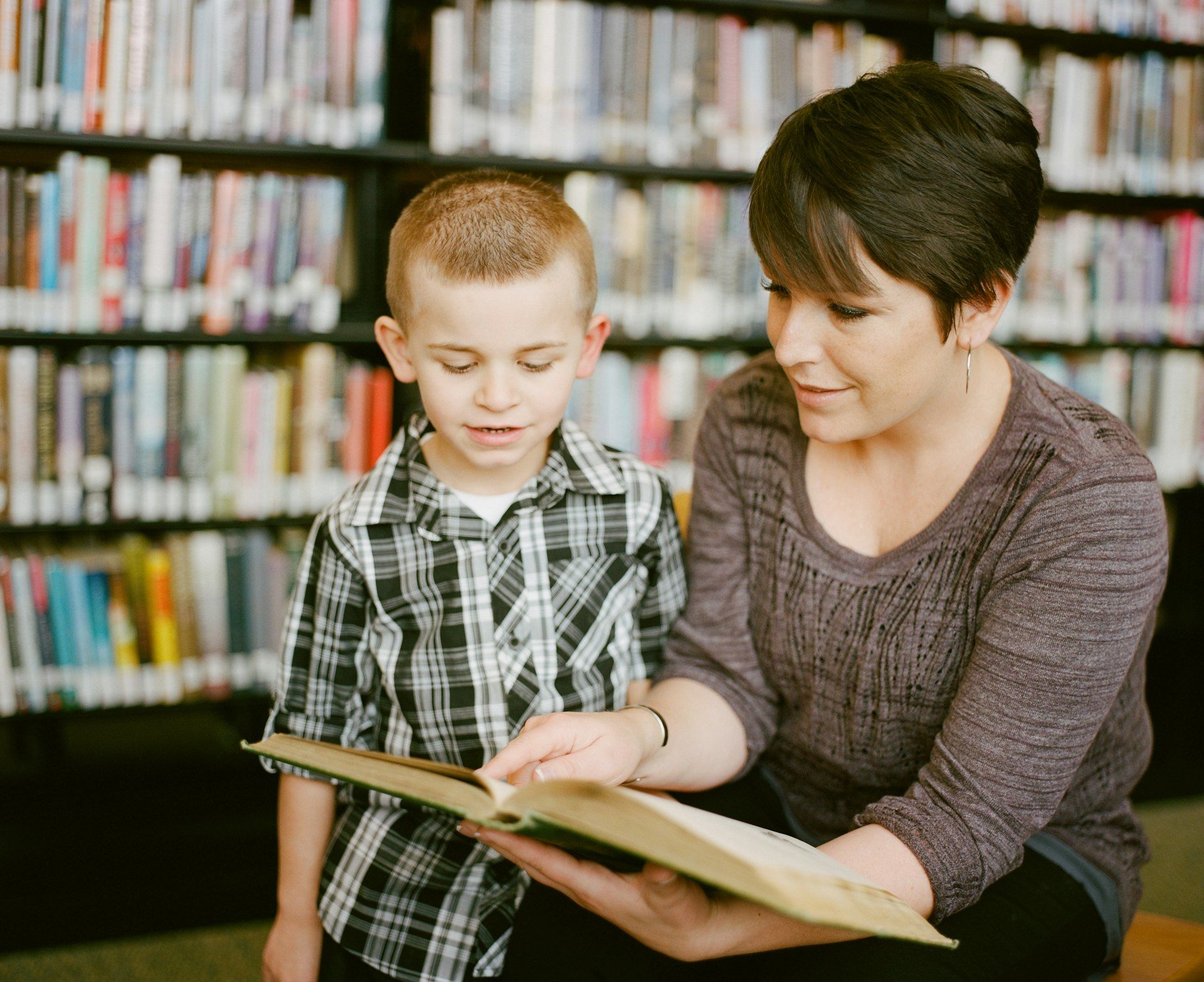 A mother reading a picture book with her young son in a library