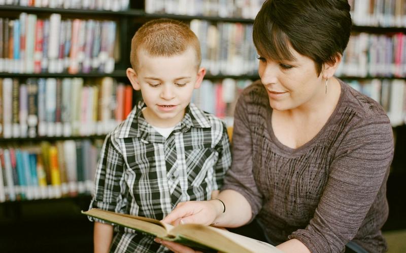 A mother reading a picture book with her young son in a library