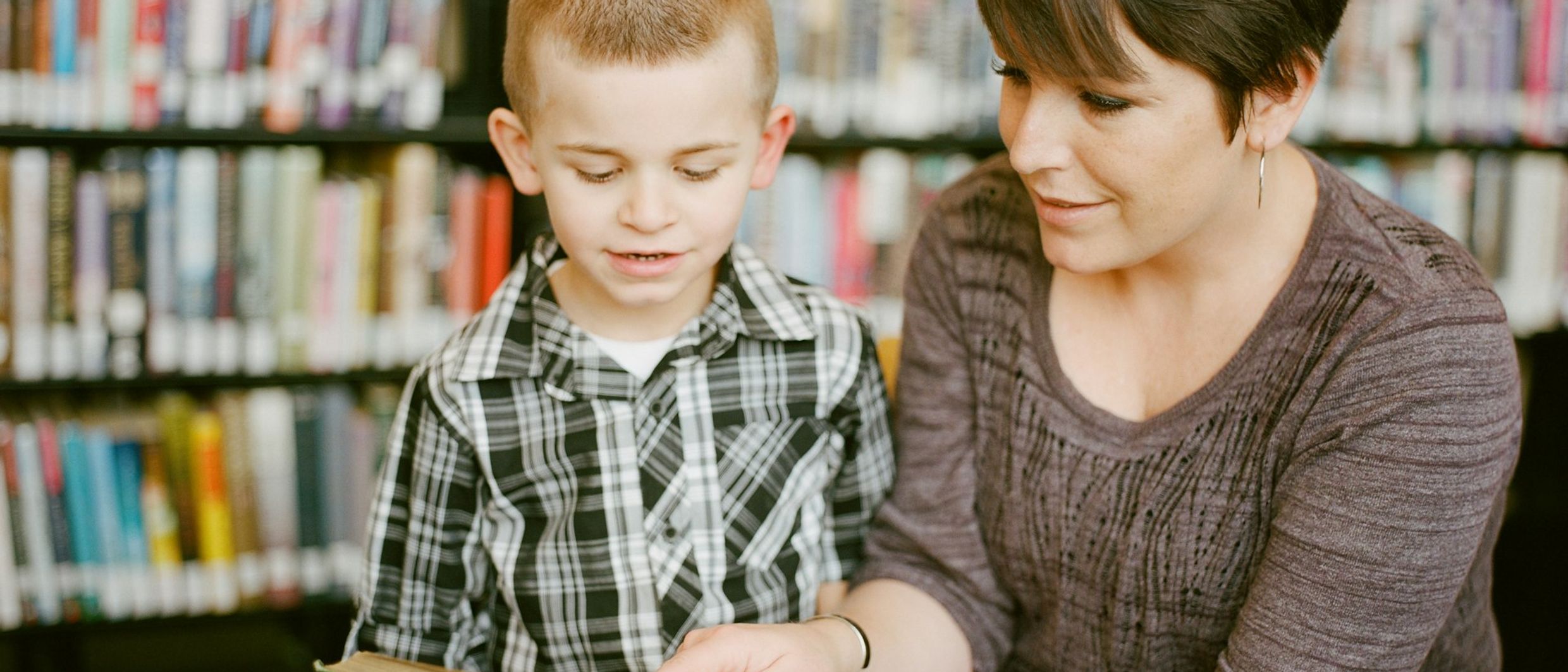 A mother reading a picture book with her young son in a library