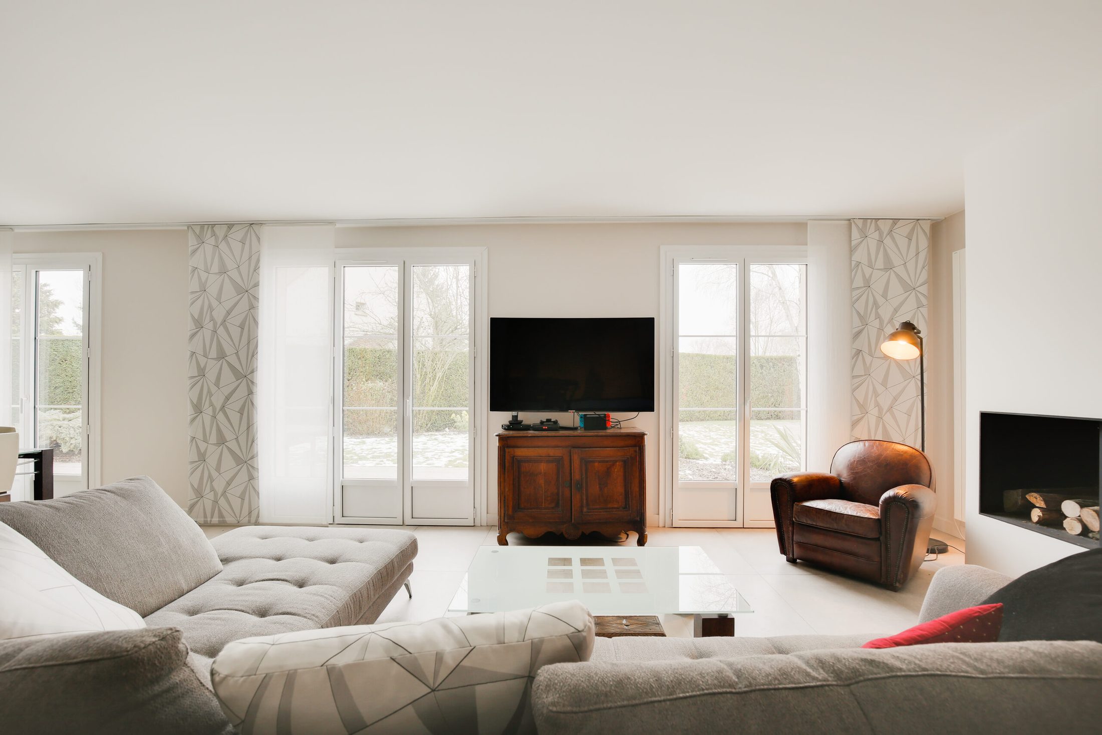 Salon de maison rénovée avec cheminée contemporaine, canapé gris et fauteuil cuir