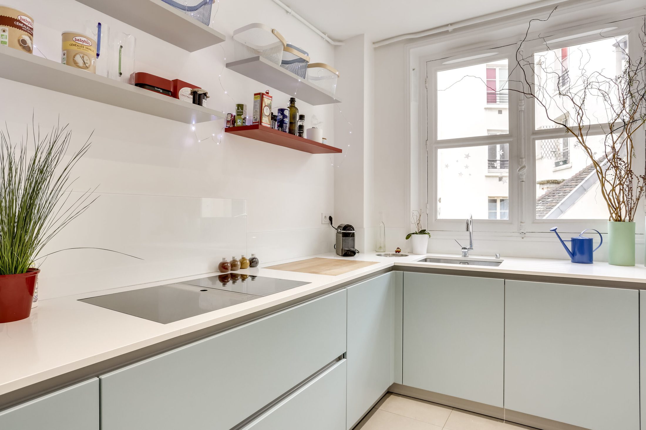 Cuisine compacte minimaliste avec armoires bleu clair et plans blancs, adaptée à un appartement