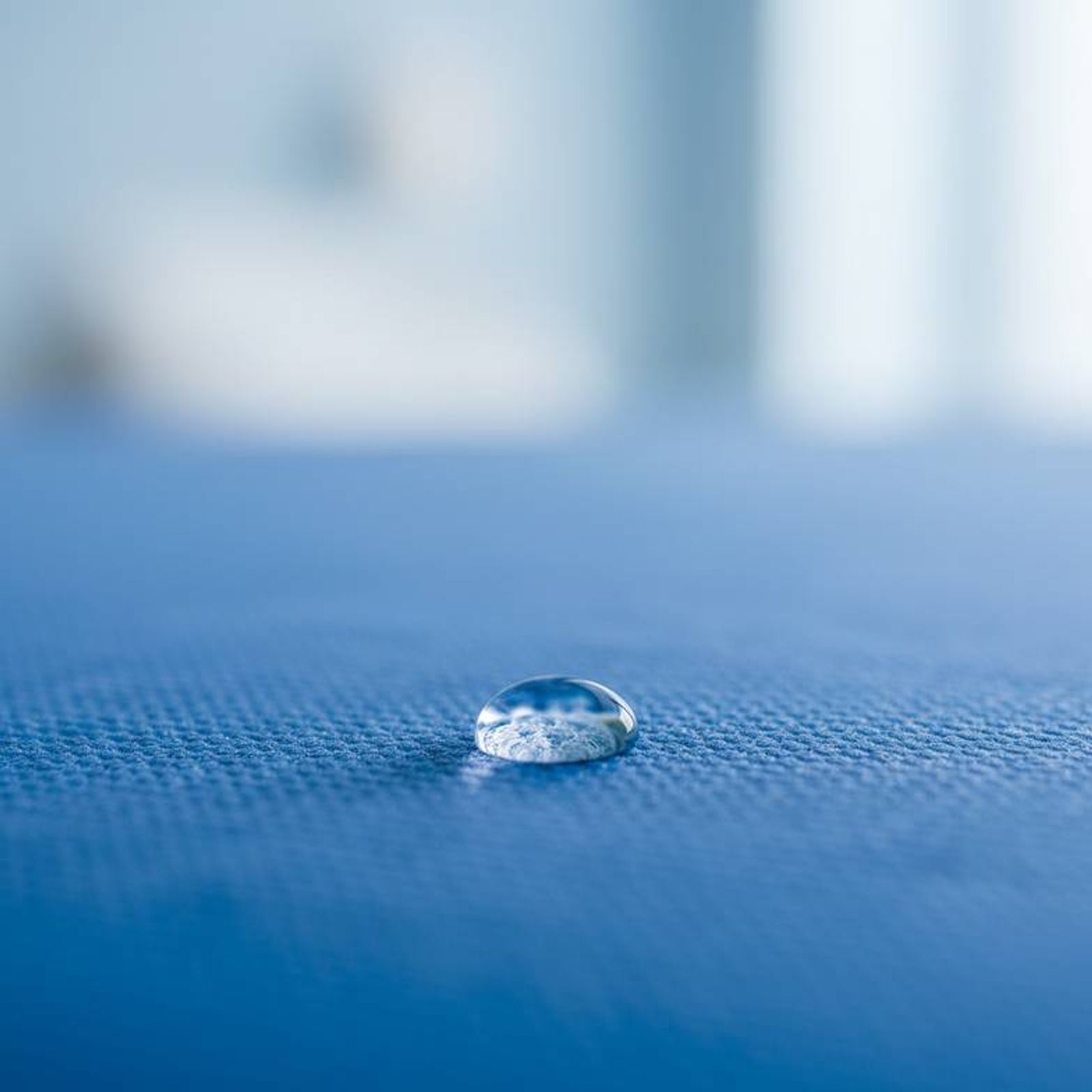 A close-up shot showing the texture of a high-quality waterproof mattress cover, with a single drop of water beading on the surface to demonstrate its function.