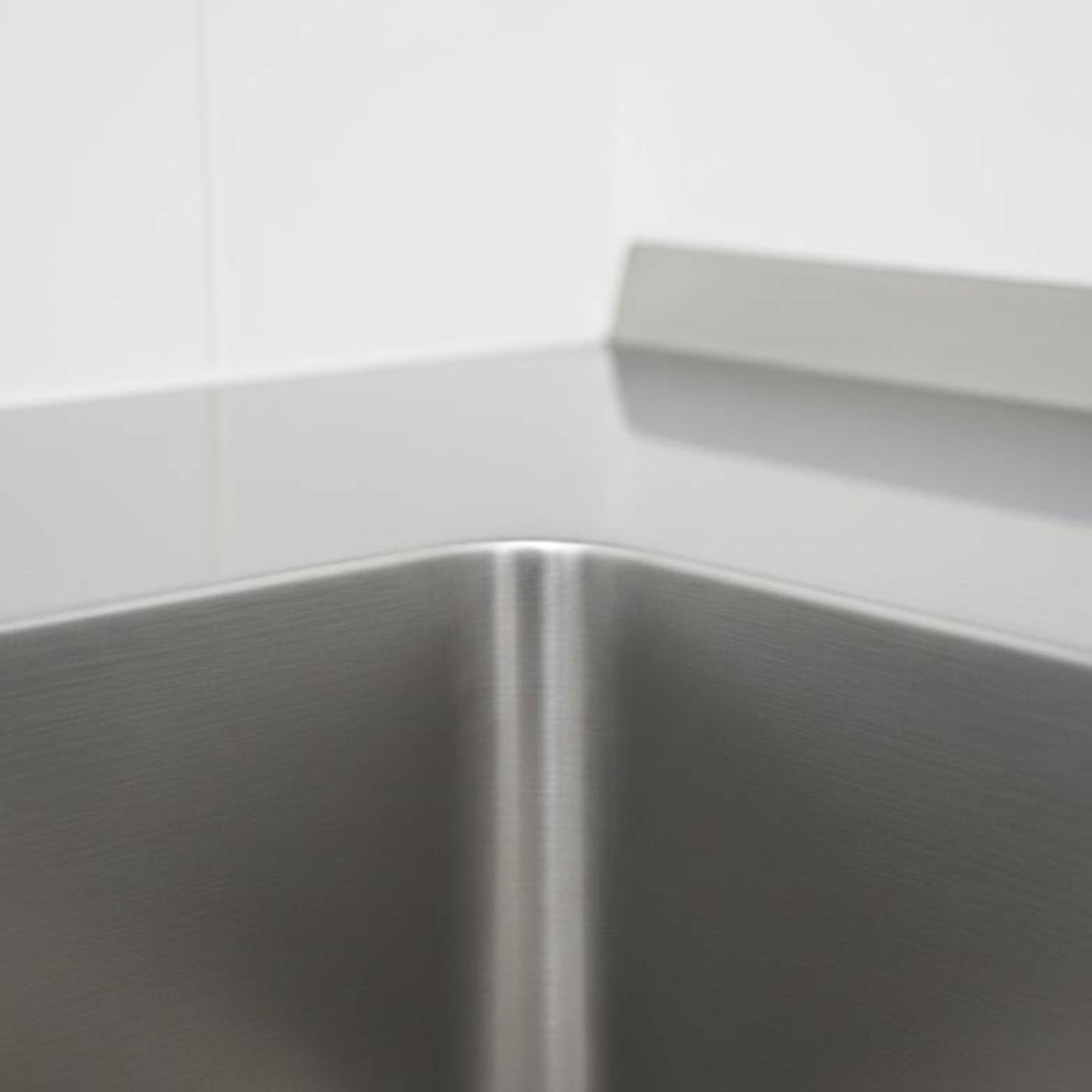 Close-up of a seamless, coved corner inside a stainless steel sink, showing it is easy to clean.