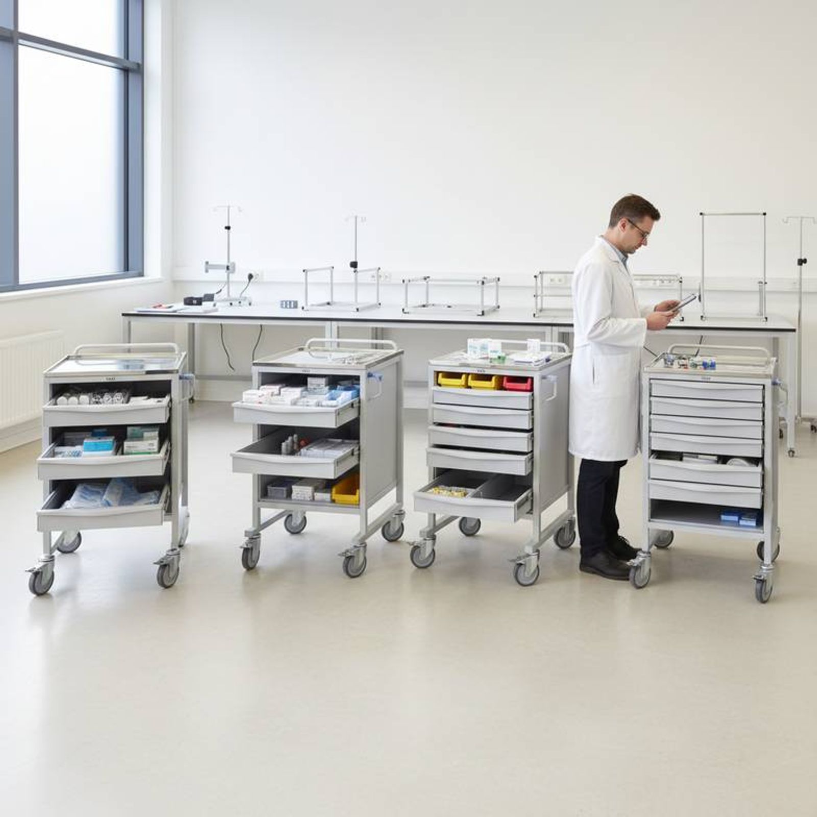 A nurse using a 3-drawer trolley for a medication round in a hospital hallway
