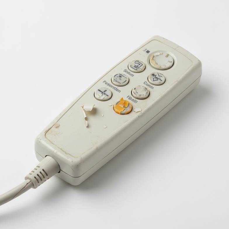 A worn-out hospital bed hand control with peeled labels and a frayed cable.