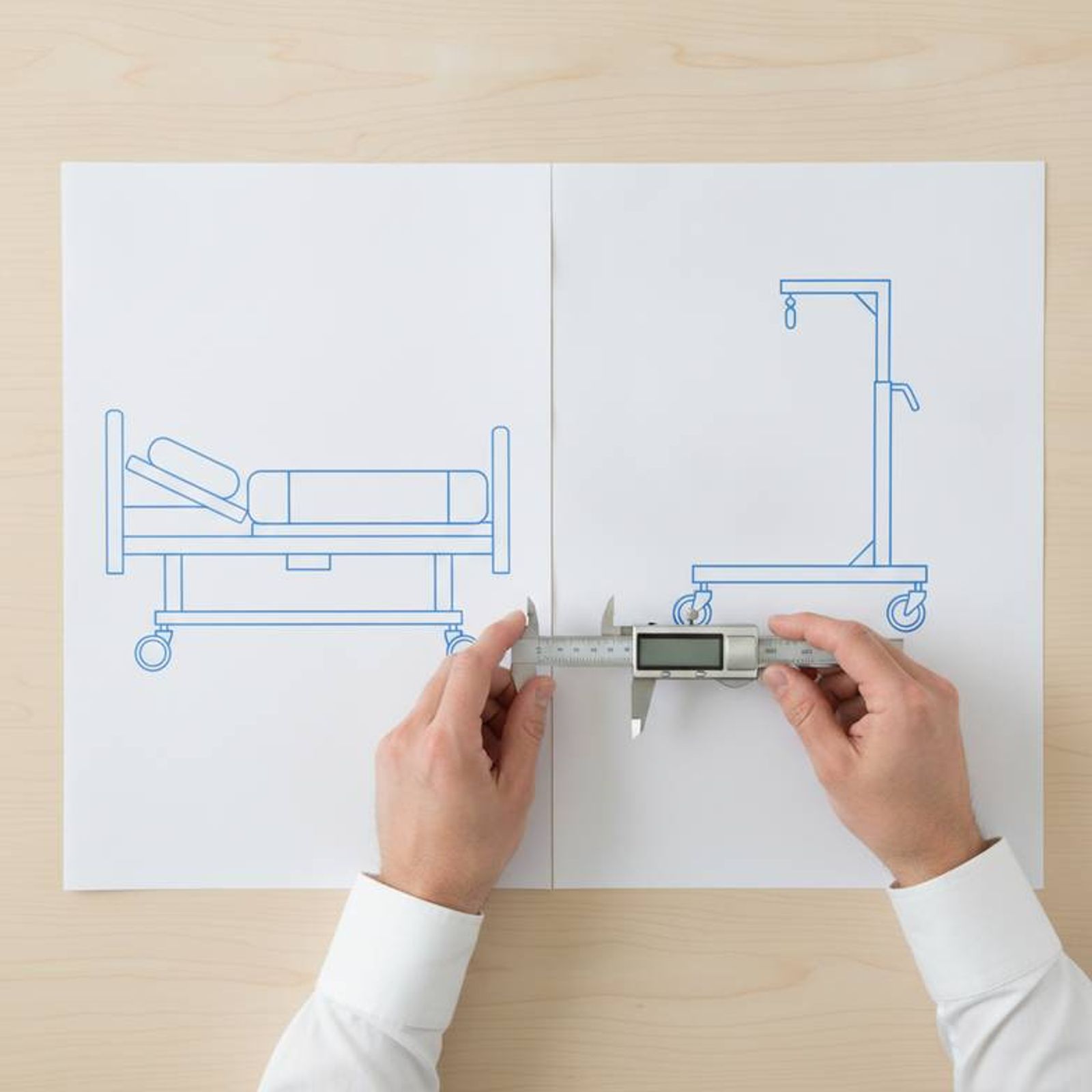 A project manager reviewing technical drawings of a hospital bed and a patient hoist side-by-side.