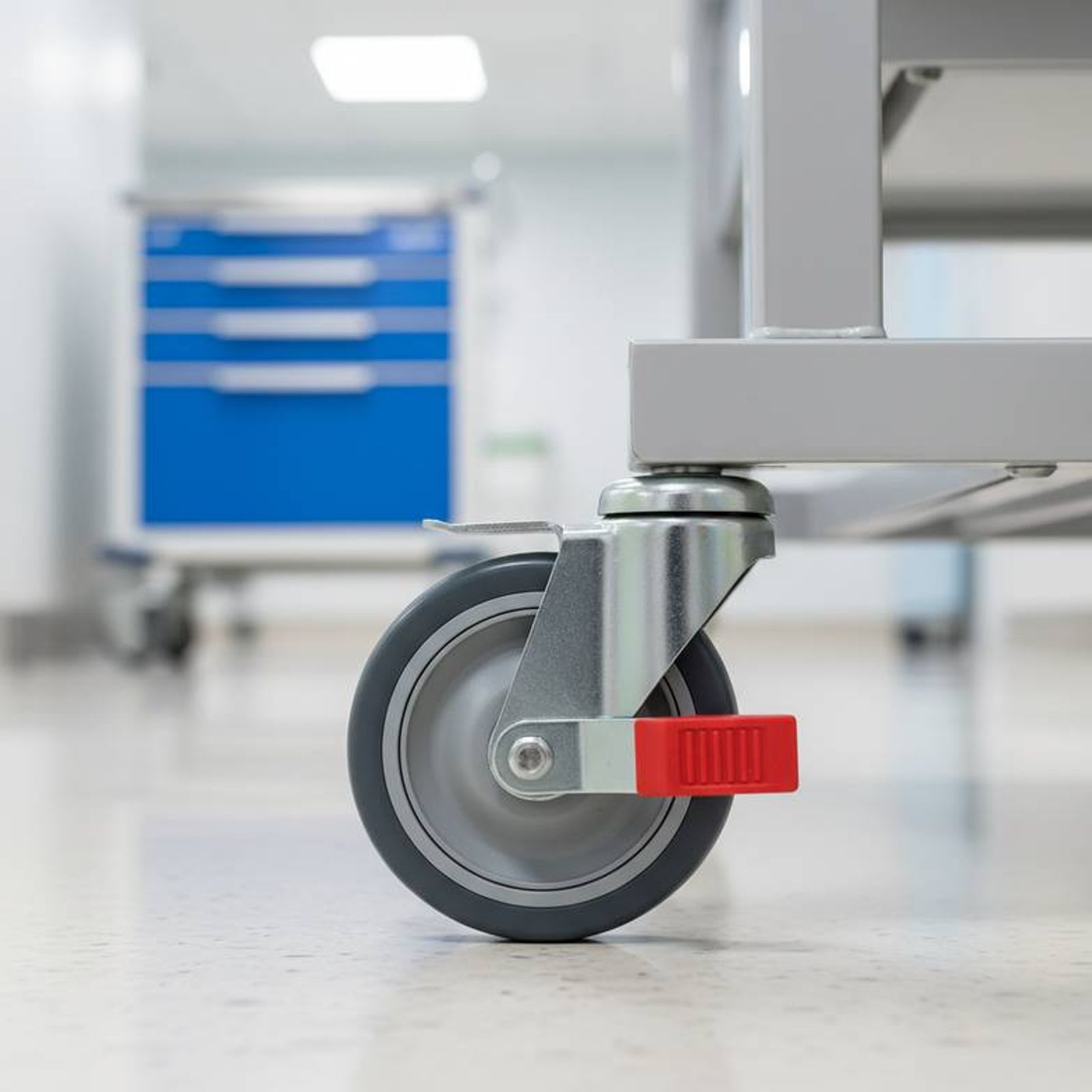 A detailed close-up of a medicine trolley's high-quality, non-marking caster with a clearly visible foot-operated brake mechanism.