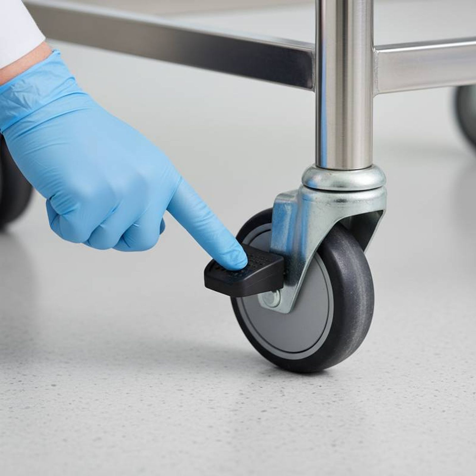 A quality inspector's hand pointing to the pedal on a medical trolley caster.